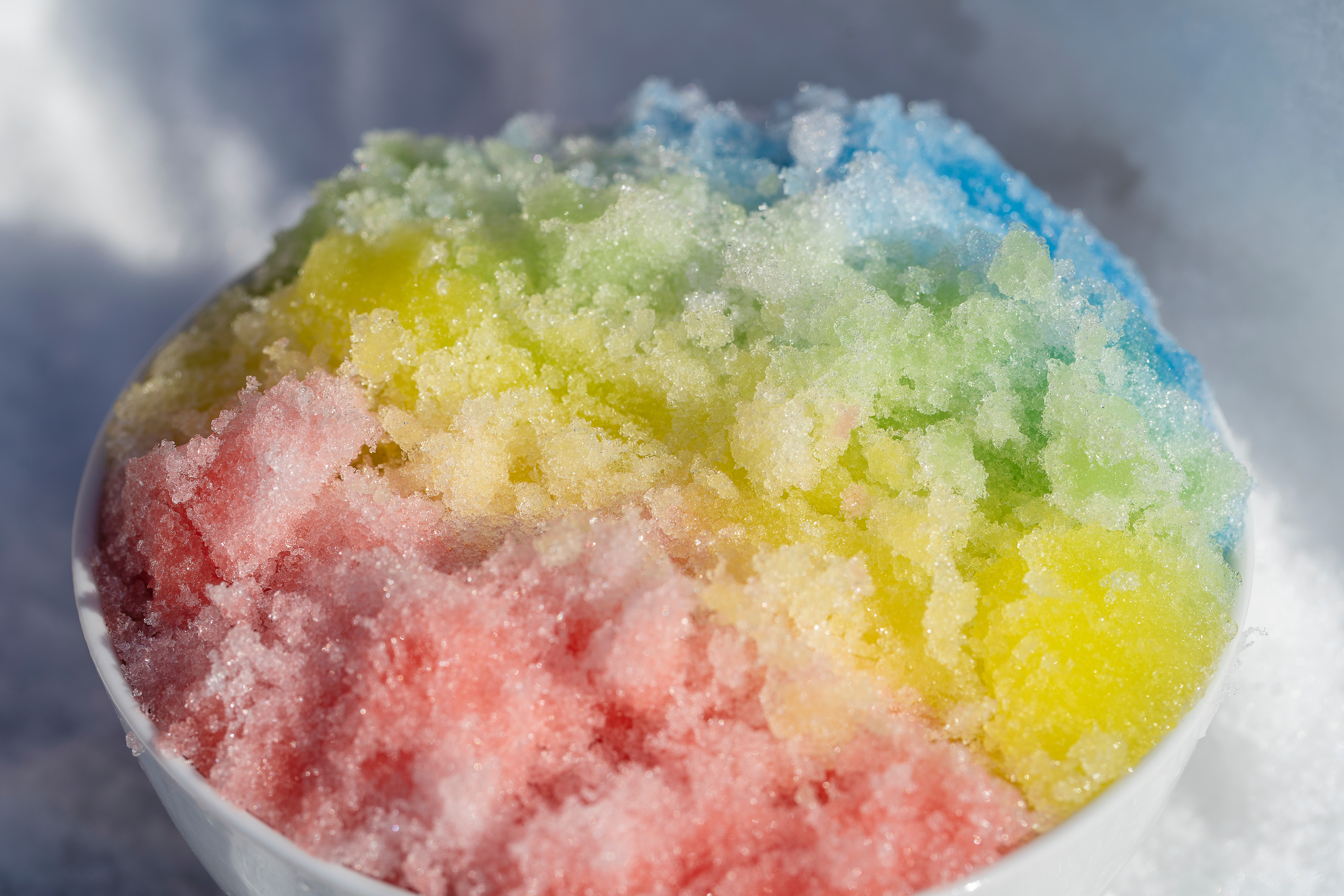 Rainbow shaved ice in dessert bowl on white snow background in winter, close up